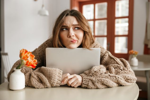 Imagem de uma mulher com expressão de insatisfação com o rosto em cima da tela do laptop