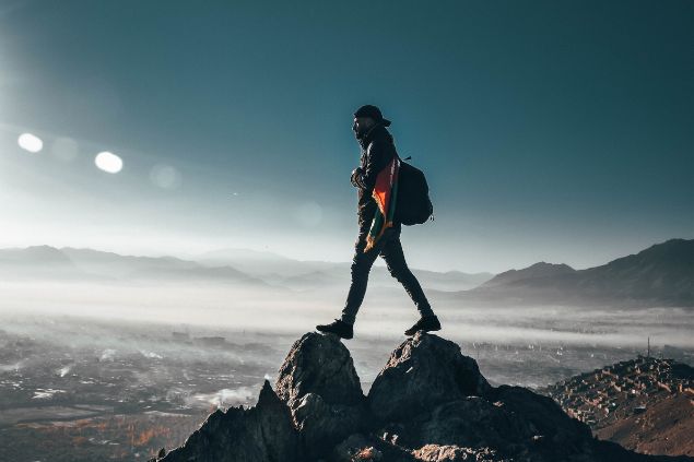 Imagem de um homem em cima de um penhasco, entre as montanhas