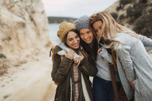 Imagem de 3 amigas abraçadas em uma estrada de terra