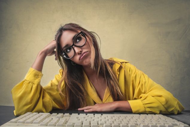 Mulher de frente para um teclado de computador, mas com feição de tédio