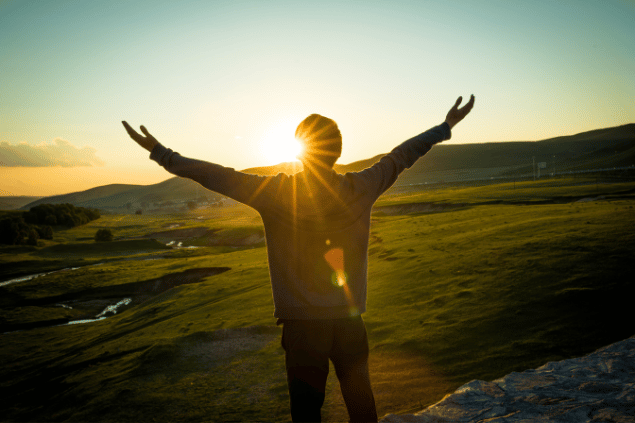 Homem com os braços abertos olhando um pôr-do-sol