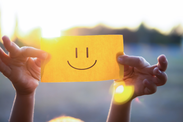 Pessoa segurando um pedaço de papel amarelo com um sorriso desenhado