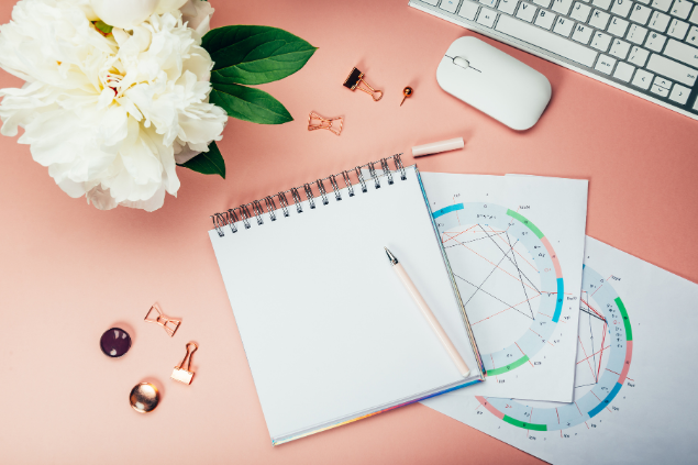 Mapas astrais em cima de uma mesa com computador, caderno e flores