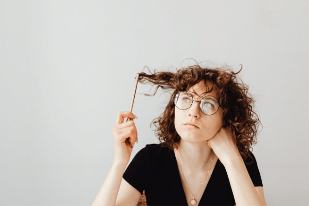 Mulher branca de cabelos curtos e enrolados mexendo no cabelo com um lápis de escrever