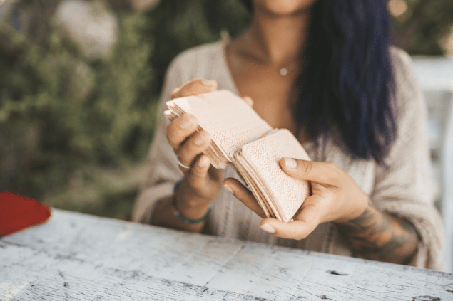 Uma mulher segura e embaralha cartas de um baralho perto de uma mesa. Ela está ao ar livre.