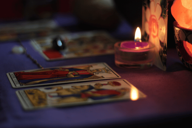 Quatro cartas de tarot estão sobre uma mesa. Duas delas estão no foco da imagem. Há uma vela acesa na mesa.