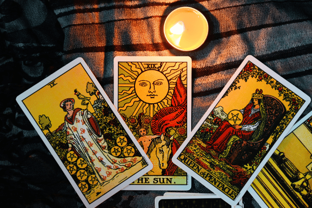 Três cartas de Tarot estão dispostas sobre uma mesa. Ao lado, há uma vela.