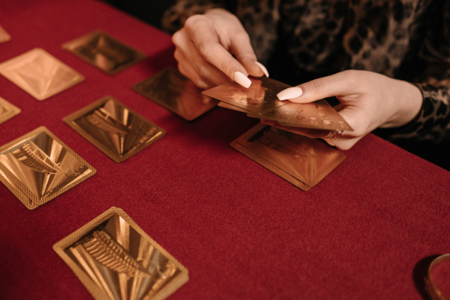 As mãos de uma taróloga segurando cartas de Tarot viradas para baixo estão em destaque na imagem.