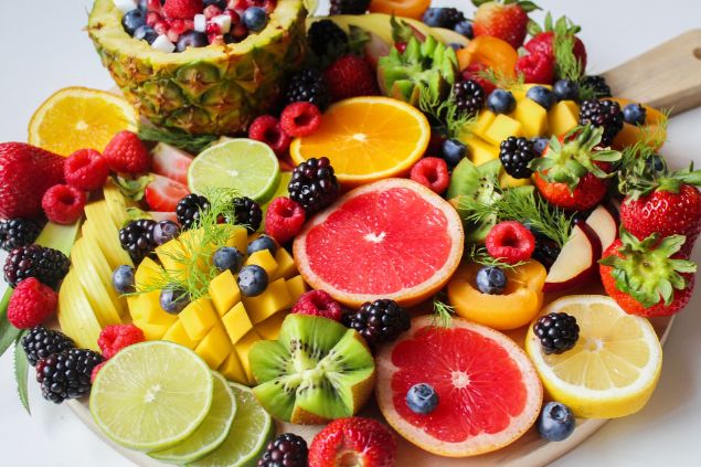 Imagem de uma tábua de madeira redonda contendo vários tipos de frutas coloridas, um dos itens de oferenda para o Exu Mirim.