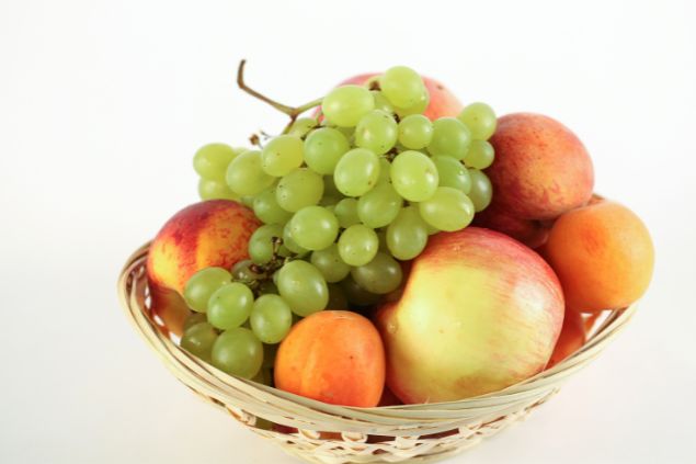 Imagem de uma cesta de vime contendo uvas, maçãs e pêssegos, uma das oferendas para o cigano Wladimir da Umbanda.