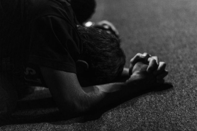 Imagem de um homem debruçado no chão com as mãos unidas em sinal de oração.
