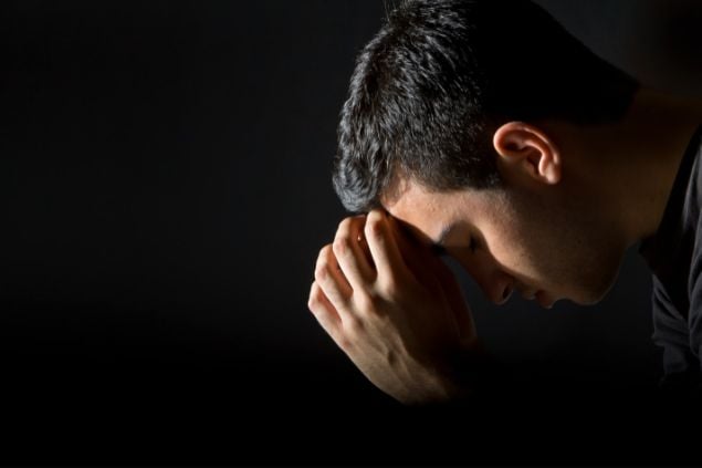 Imagem de um homem ajoelhado com as mãos sobre o rosto em sinal de oração.