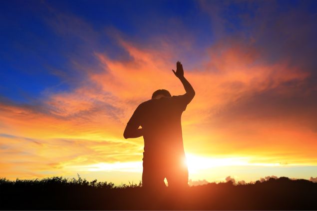 PonyWang / Getty Images Signature / Canva Imagem de fundo de um lindo pôr do Sol e em destaque um homem ajoelhado com uma de suas mãos para o alto, em oração.