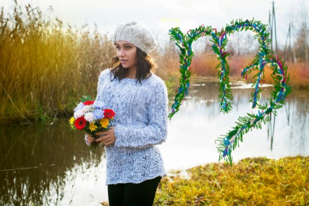 Dzhulbee / Getty Images / Canva Imagem de uma mulher segurando um arranjo de flores do campo coloridas e ao lado, o glifo do signo de virgem.