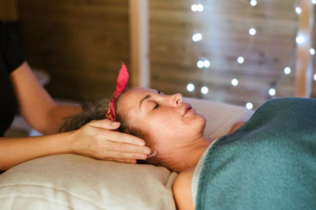 Imagem de um reikiano aplicando reiki em uma paciente deitada sobre uma maca.