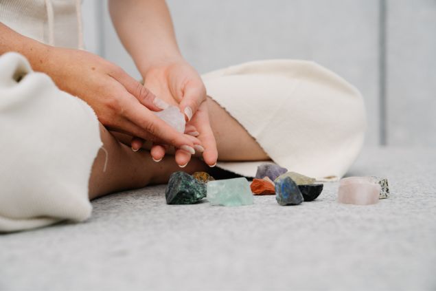 Imagem de uma reikiana sentada sobre um tapete branco, manipulando alguns cristais e pedras para renovar suas energias para a prática do reiki.