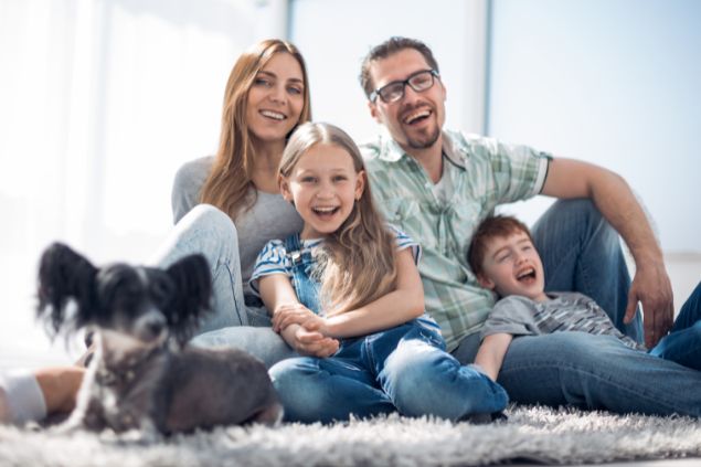 Imagem de uma famlília feliz, reunida em uma sala de estar. Todos estão sentados em um tapete, simbolizando o signo de câncer.
