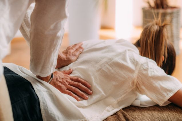 Imagem de uma mulher desfrutando de massagem shiatsu nas costas, deitada em um tapete de massagem.