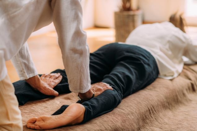 Imagem de uma mulher deitada de bruço em um tapete recebendo Massagem Shiatsu