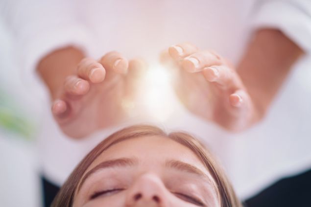 Imagem da cabeça de uma mulher recebendo as energias das mãos de uma mulher durante a prática do Reiki.