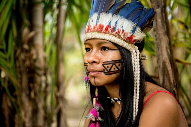 Imagem de uma mulher com traços indígena, usando cocar e rosto pintado em uma floresta, representando a cabocla Jurema, guardiã das florestas.