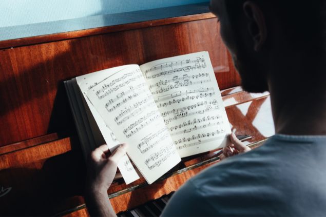 Imagem de um homem  lendo algumas partituras em sala de aula, uma das habilidades do signo de virgem.