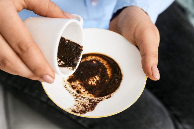 Imagem das mãos de uma mulher segurando uma xícara e um pires branco. Ela está fazendo a leitura da borra do café - cafeomancia.