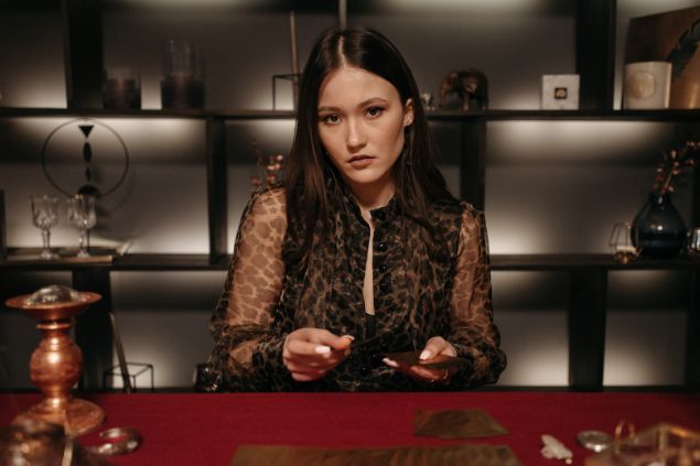 Imagem de uma mulher de cabelos longos. Ela é uma cartomante e está tirando cartas para uma consulente.