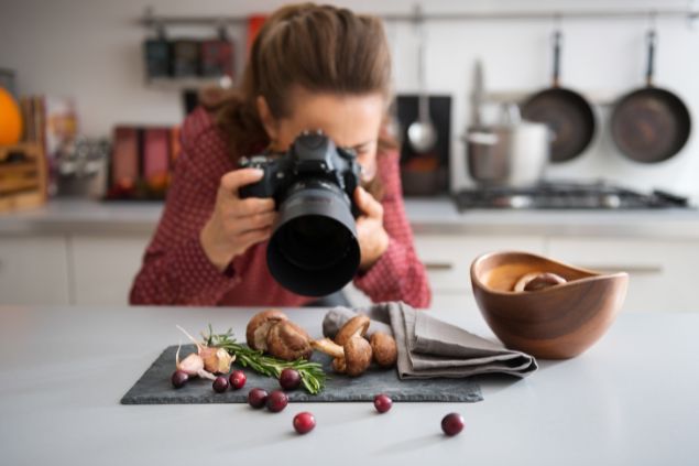 Imagem de uma mulher publicitária uma cozinha fazendo fotos de ingredientes para um prato culinário de uma campanha.