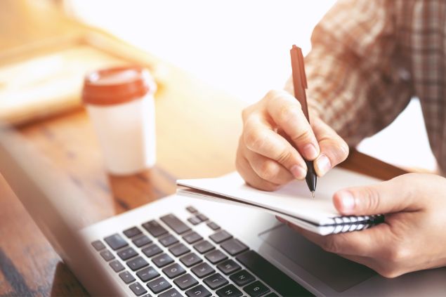 Imagem de um analista de estatísiticas trabalhando. Sobre sua mesa, papéis, computador e calculadora.