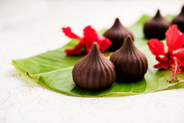 Imagem de uma oferenda de doces para os Erês, feita com folha de bananeira e uma flor vermelha de hibisco.