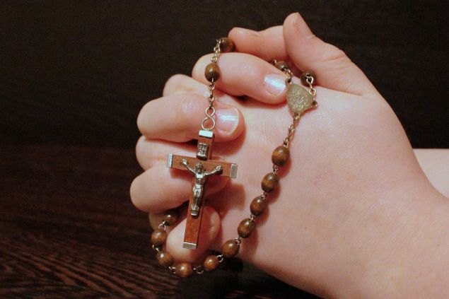Imagem das mãos de uma mulher segurando um terço. Ela está rezando como forma de fazer a sua limpeza espiritual.