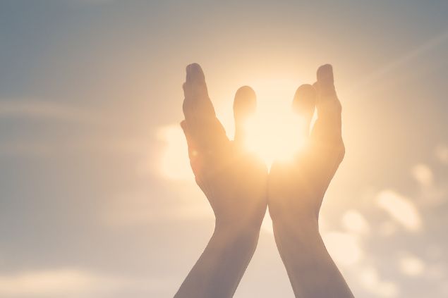 Imagem da mão de uma pessoa segurando o sol na palma, sentindo-se energizada. Conceito espiritual, mente e corpo.
