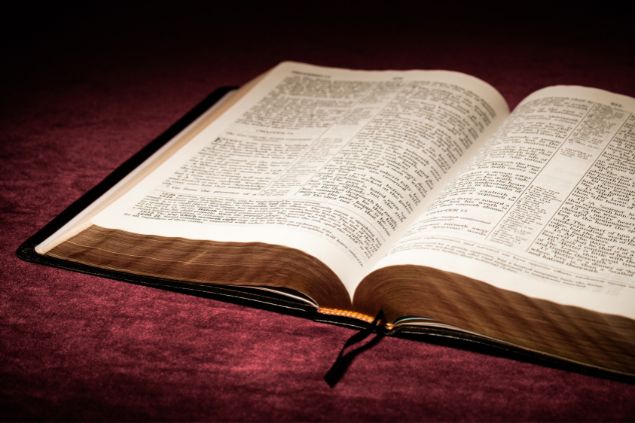 Imagem da Bíblia - livro sagrado do Cristianismo. Ela está aberta sobre um tecido de cor vinho.