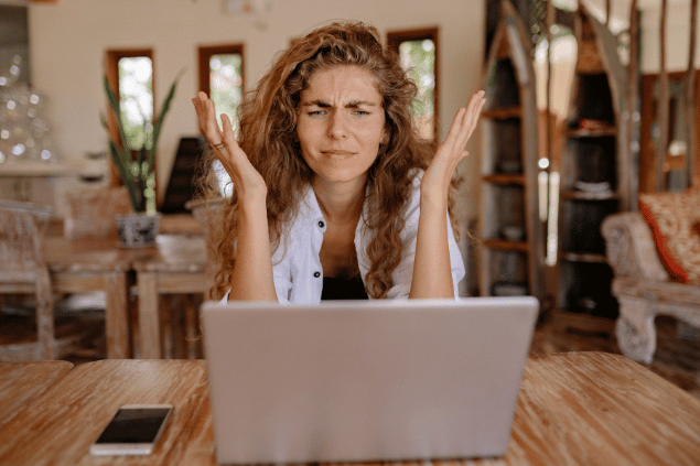 Mulher irritada olhando para o notebook em cima de uma mesa de madeira