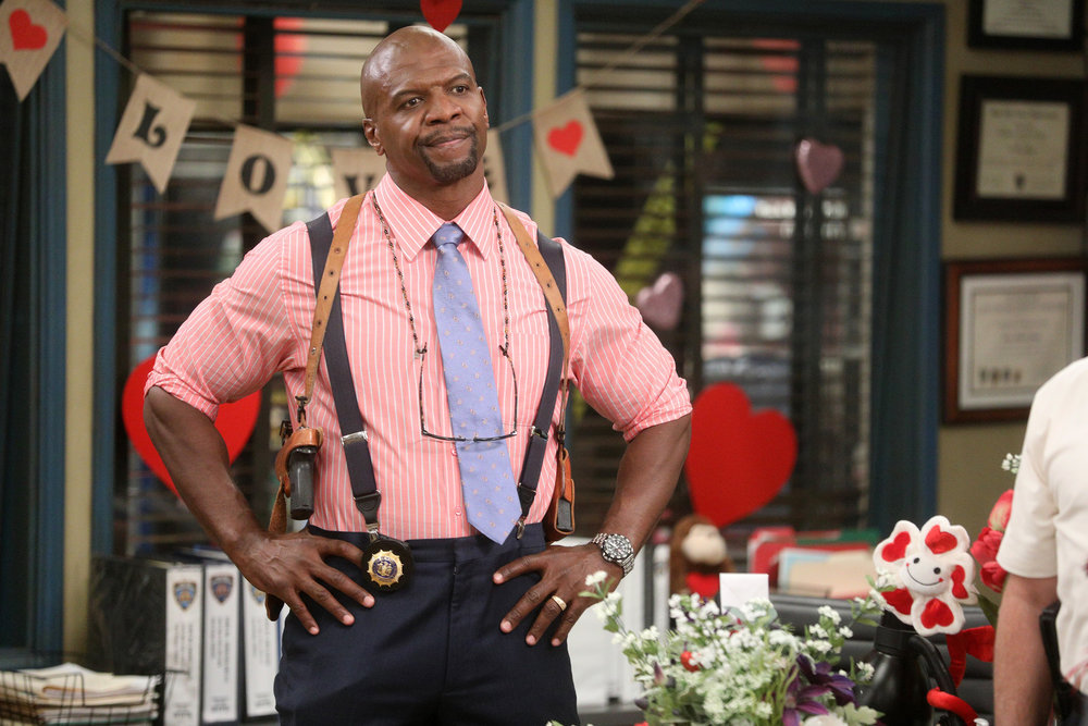 Homem negro vestido camisa rosa de listras e gravata azul, com mãos na cintura e expressão convincente.