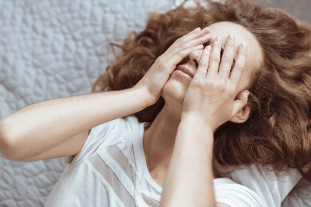 Mulher com as mãos sobre o rosto, sentindo-se estressada e com dores. Conceito de pensamentos negativos. 