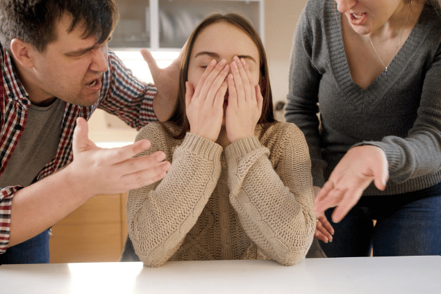 Garota com as mãos no rosto enquanto pais discutem com ela. Conceito de problemas familiares. 