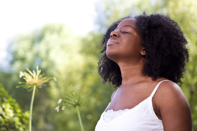 Digitalskillet / Getty Images Signature / Canva Uma mulher está em um ambiente de natureza. Ela levanta a cabeça, fecha os olhos e sente os raios de sol na pele.