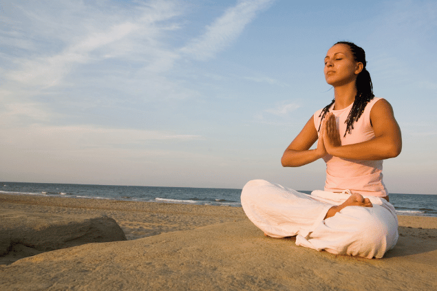 Uma mulher está sentada e meditando na praia sob a luz do sol.