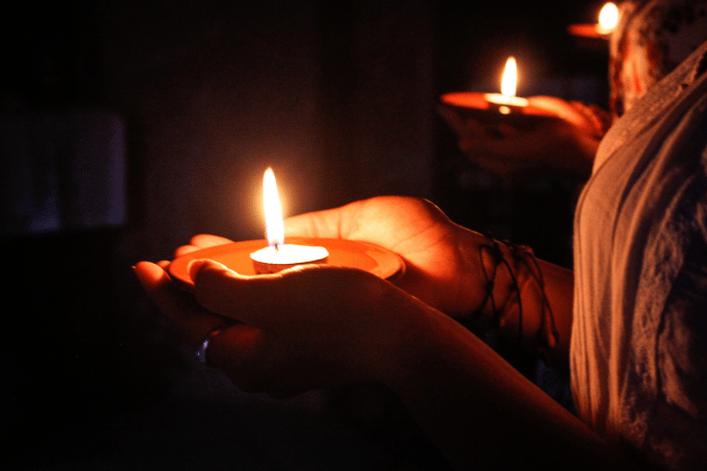 Três mulheres seguram uma vela acesa cada em um prato.