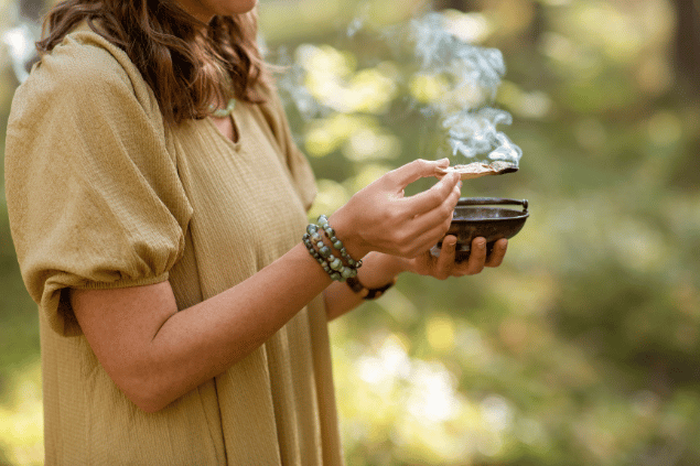 Uma mulher está queimando palo santo em um ambiente de natureza.