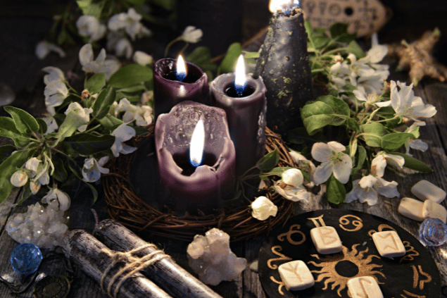 Na imagem, há velas, flores e pedras em cima de uma mesa.