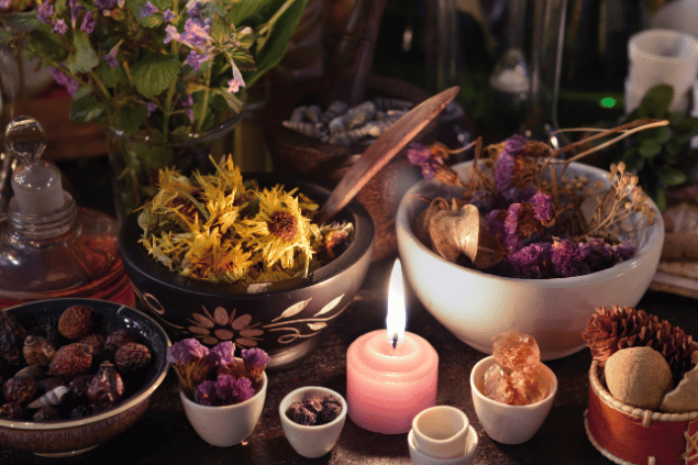 Vera Petruk / Canva Na imagem, há alguns recipientes com flores e pedras em cima de uma mesa. E há uma vela acesa.
