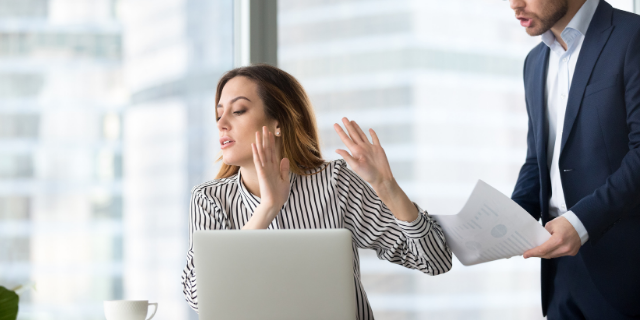 Mulher sentada à mesa do trabalho recusa papéis que um homem entrega à ela.
