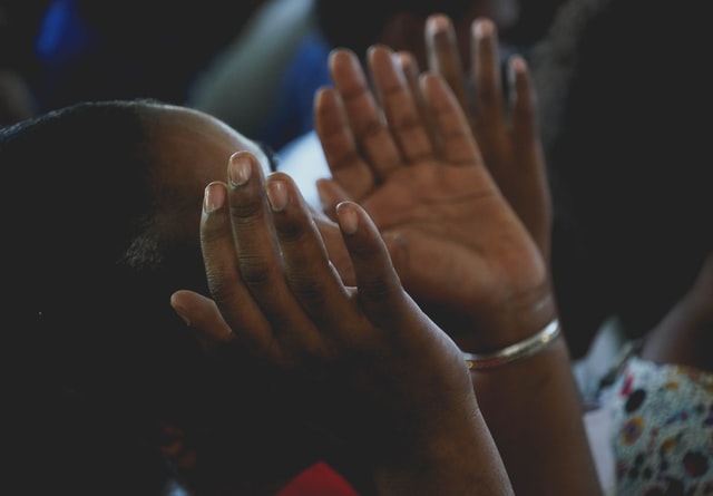 Mulher negra de mãos abertas levantadas.
