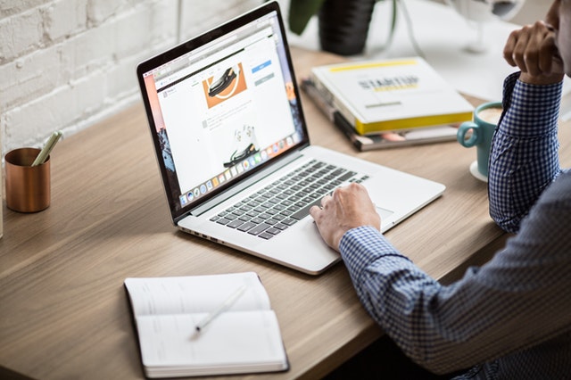 Braços de homem trabalhando em notebook sobre a mesa com itens na mesa
