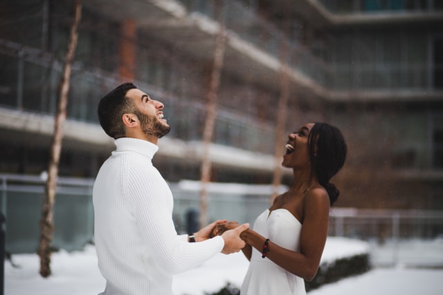 Homem branco e mulher negra com roupas brancas, olhando para cima.