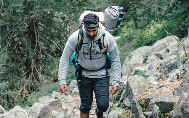 Homem branco subindo morro com mochila nas costas.