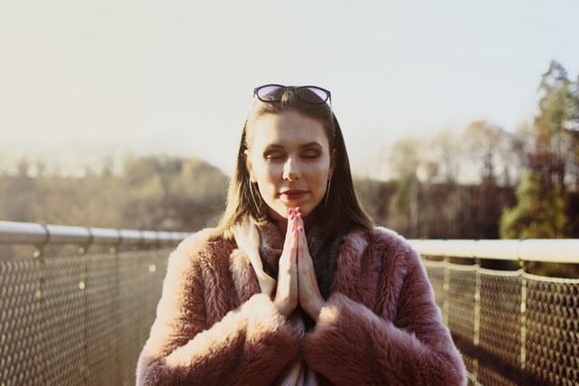 Mulher branca de mãos juntas e olhos fechados.
